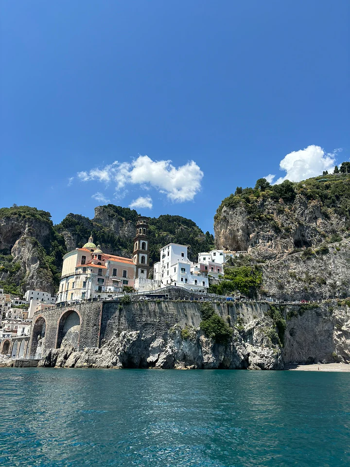 A pastel village stacked on cliffs above clear green water on the Amalfi coast.