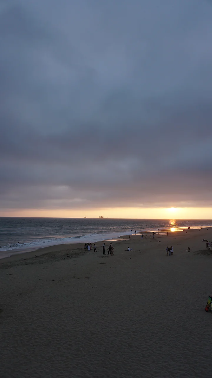 The sun dropping to the horizon over a wide, near-empty beach.