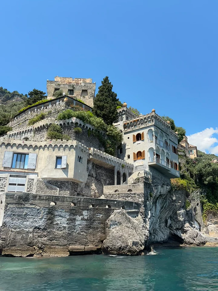 An old villa built into a cliff face directly above turquoise sea.