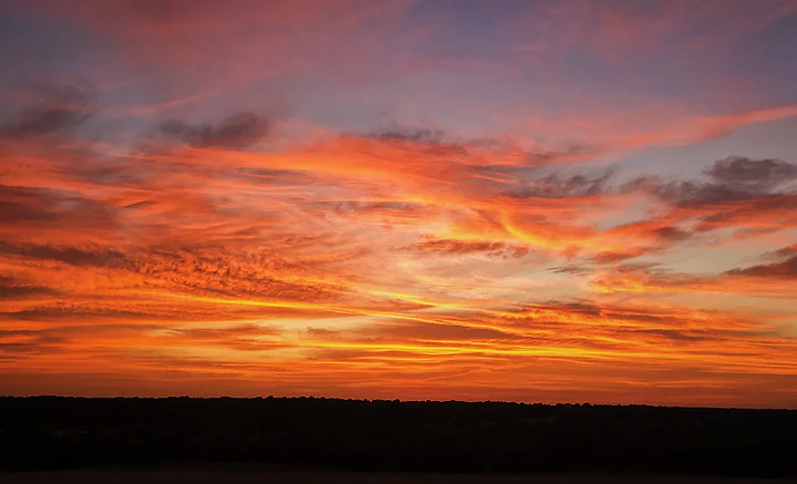 A sky of deep orange and red cloud burning above a dark treeline.