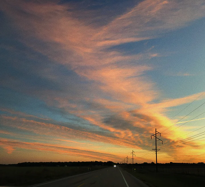 Teal and orange sunset over a straight highway lined with power poles.