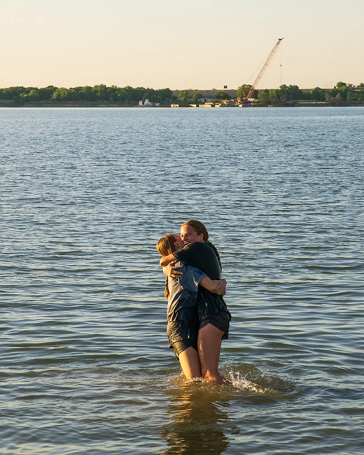 One person lifts another off their feet in a hug in the lake shallows.