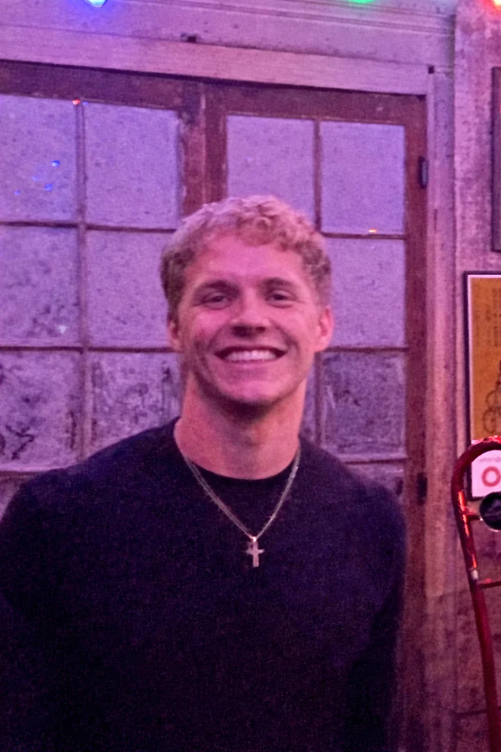 A portrait of Miles smiling, lit in warm magenta light.