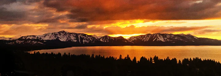 A dark mountain range in panorama beneath a burning orange sunset.