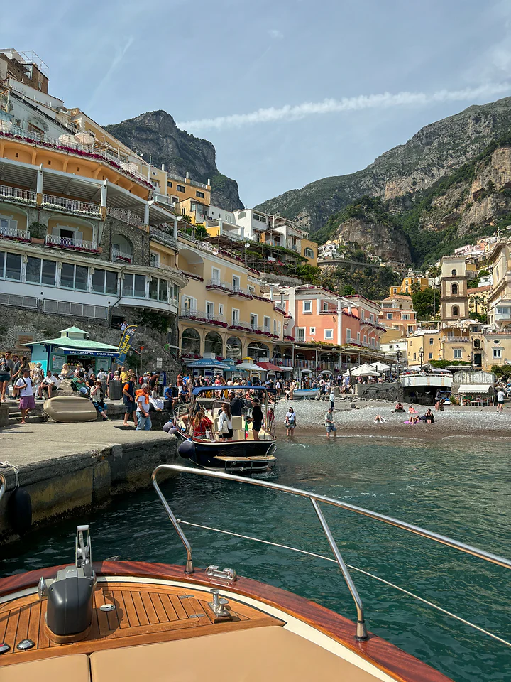 The bow of a wooden boat approaching the crowded shoreline of Positano.
