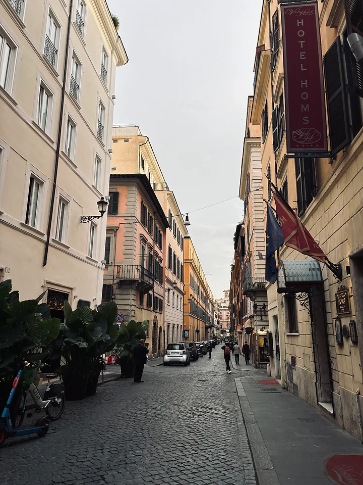 A narrow Rome street in soft evening light, shutters closed along the buildings.