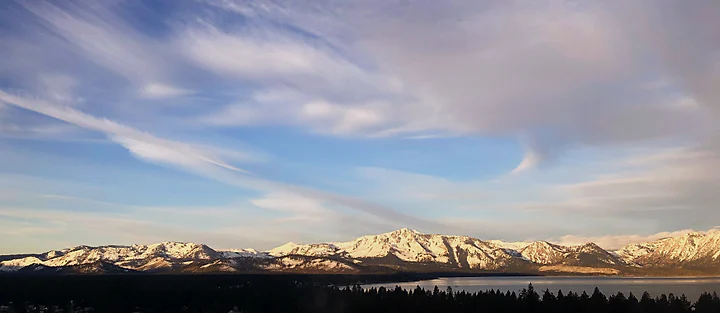 A distant snow-covered mountain range beneath wide wind-brushed cloud.