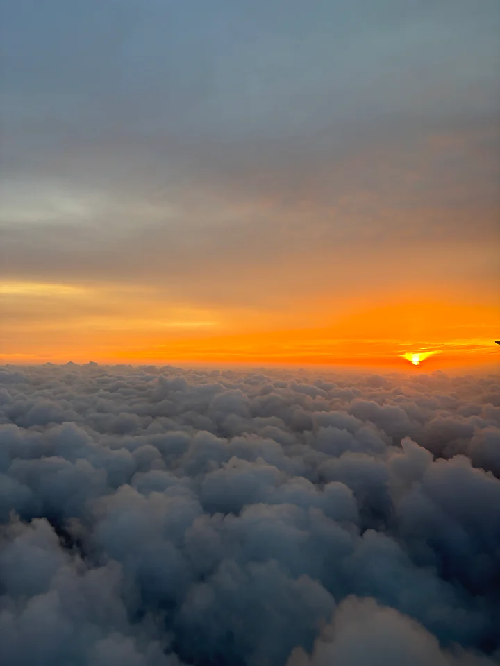 The sun sitting low over a thick, rolling bank of cloud at altitude.