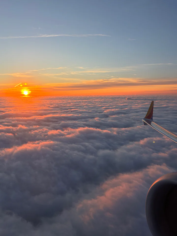Sunrise breaking over an unbroken floor of cloud, seen from a plane window.
